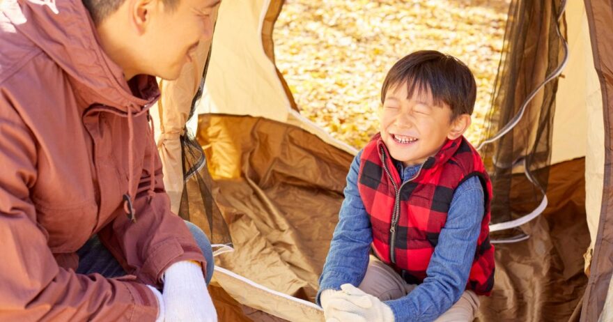 テントの中で楽しそうに笑い合う父親と子供。キャンプシーン。