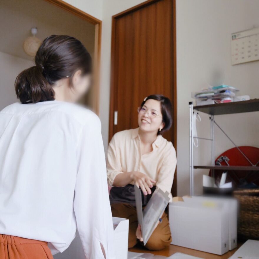 整理収納サポートの場面。1人の女性がファイルを手に笑顔で対話しています。向き合って、細やかにアドバイスしています。