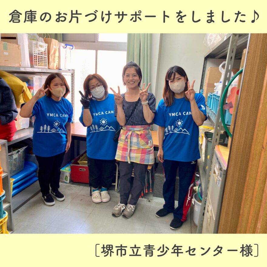 片づけを終えた倉庫の前で、整理収納アドバイザーと『YMCA CAMP』と書かれた青いTシャツを着たスタッフ4人が笑顔でピースしている集合写真。