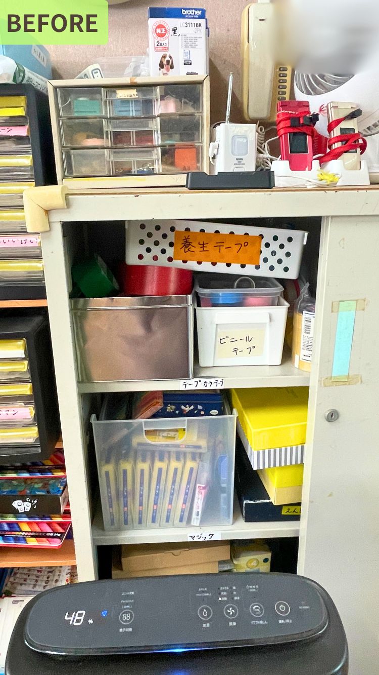 事務用品が詰め込まれた収納棚。養生テープやビニールテープ、マジックペンなどの箱やケースに分類されているが、全体的に雑な印象。